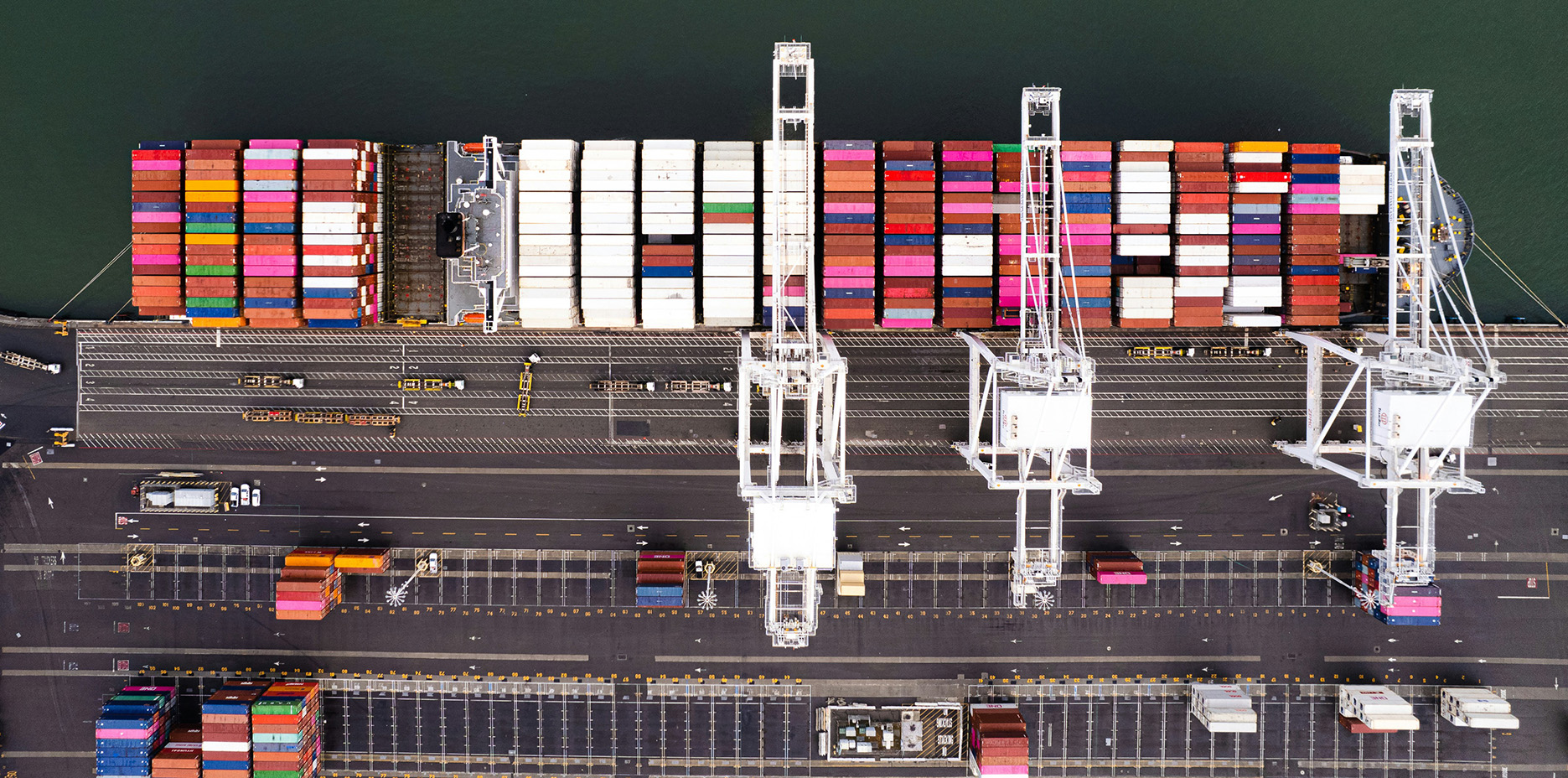 Overhead view of quay cranes, a container ship and port access lanes
